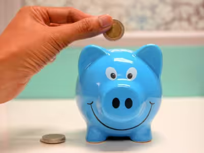 Una mano metiendo una moneda en una hucha de cerdo azul